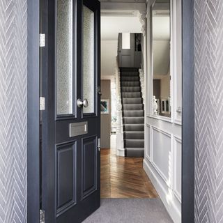 Open front door leading to hallway with classical foliate plaster decoration and staircase with textured grey carpet