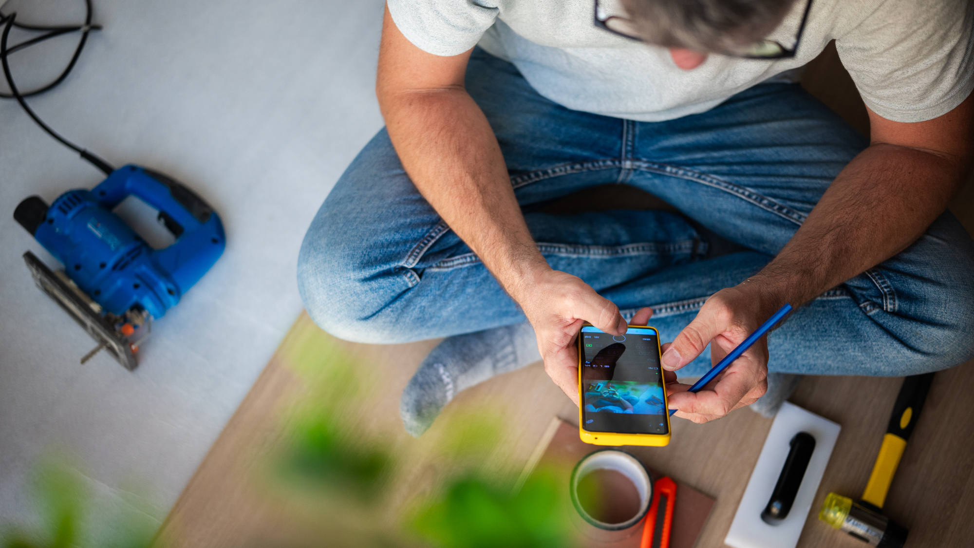 male sat on floor looking at phone with tools around him on floor