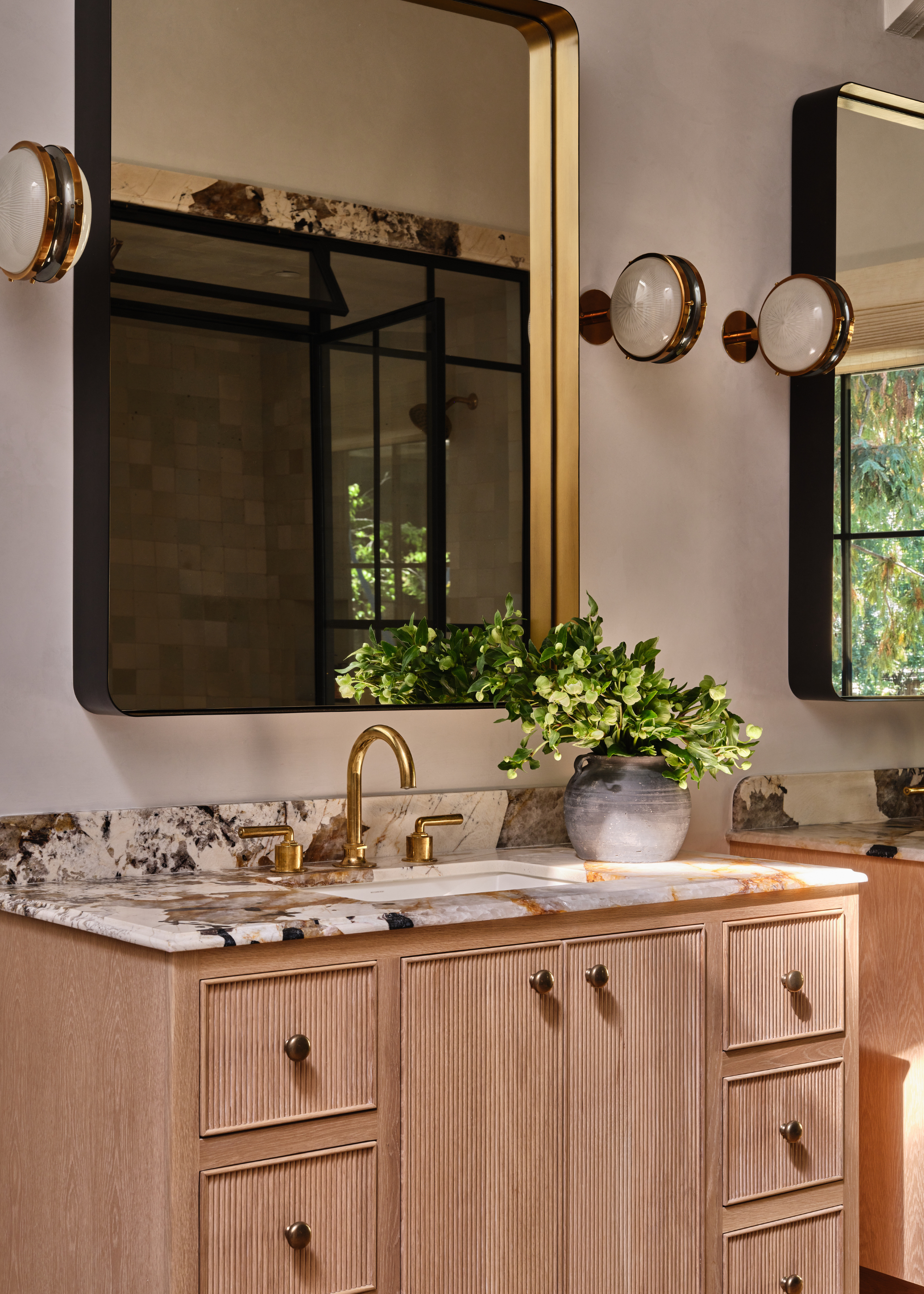 two ribbed wooden vanities with marble tops and gold sinks, with matching mirrors and wall sconces above
