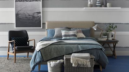 Coastal grey bedroom with striped wallpaper, fitted shelf, framed photograph,double bed, blue and grey bedlinen, vintage sidetable, wicker basket case.