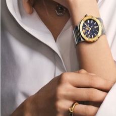 A silver, gold, and blue watch from Watch Shop on a woman's wrist
