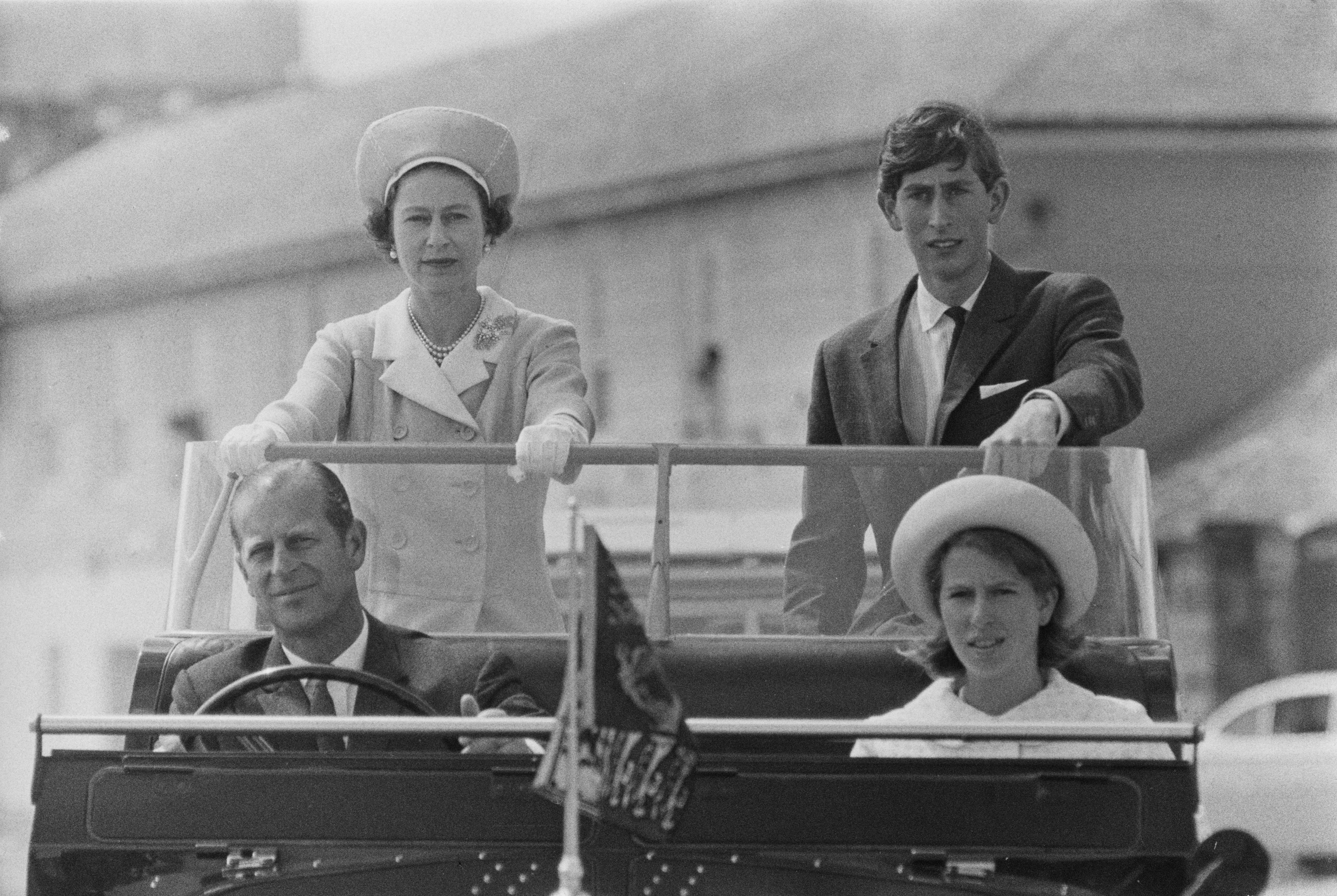 Prince Philip driving an open top jeep with Princess Anne riding in the front and Queen Elizabeth and Prince Charles in the backseat