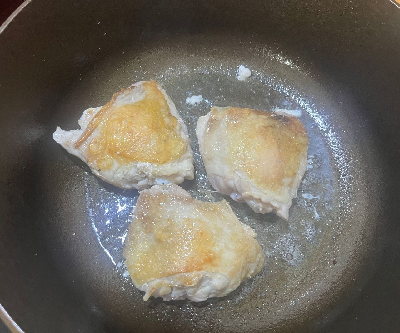 A small bronze colored cast-iron Dutch oven with golden skin-on chicken thighs inside.