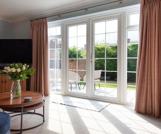 Interior view of tidy living room with light shining through clean glass doors and windows onto vase of flowers