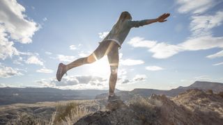 Female trail runner stretches on mountain ridge in the morning