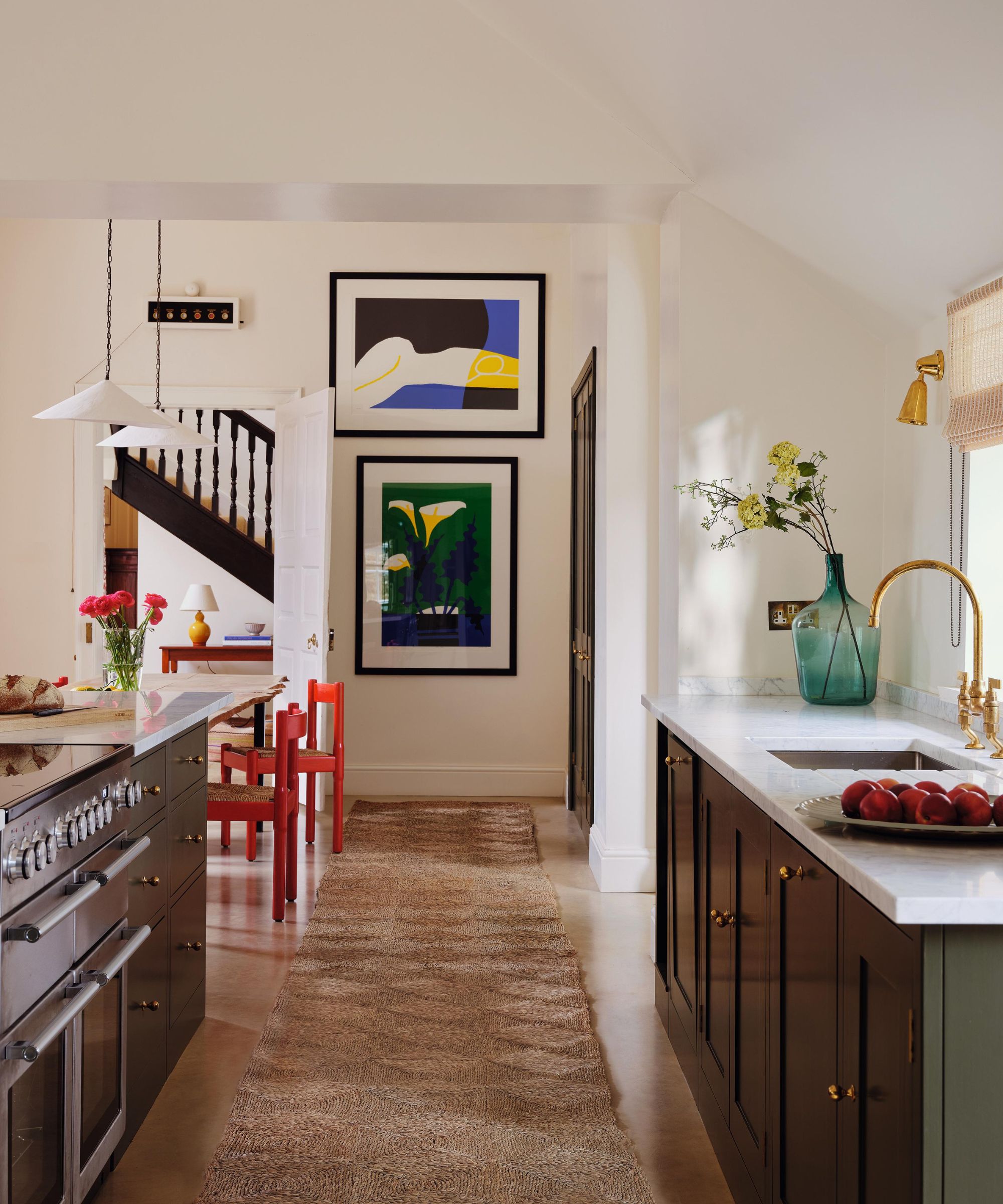 a white bright kitchen with dark green cabinetry, a central island, runner rug, abstract art and red dining chairs