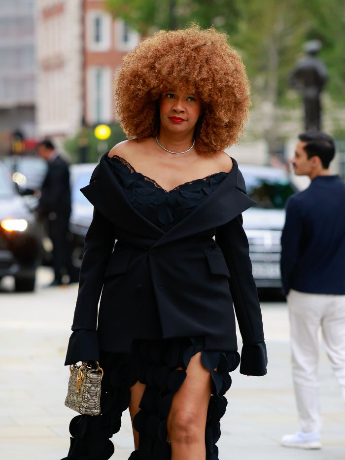 A woman at London Fashion Week wearing a black off-the-shoulder dress with copper hair