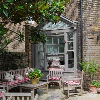 house with exposed brick walls and garden with wooden chairs and plant in pots
