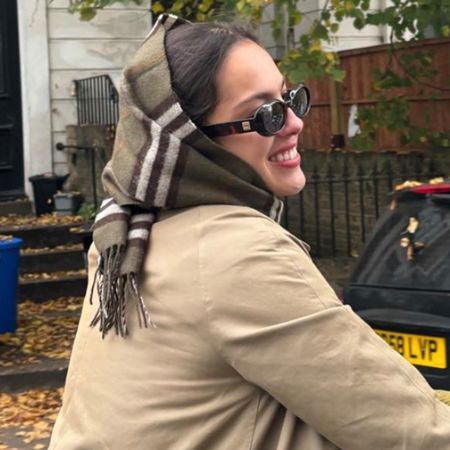 Olivia Rodrigo riding a bike in London wearing a Burberry scarf on her head with a Burberry trench coat and sunglasses.