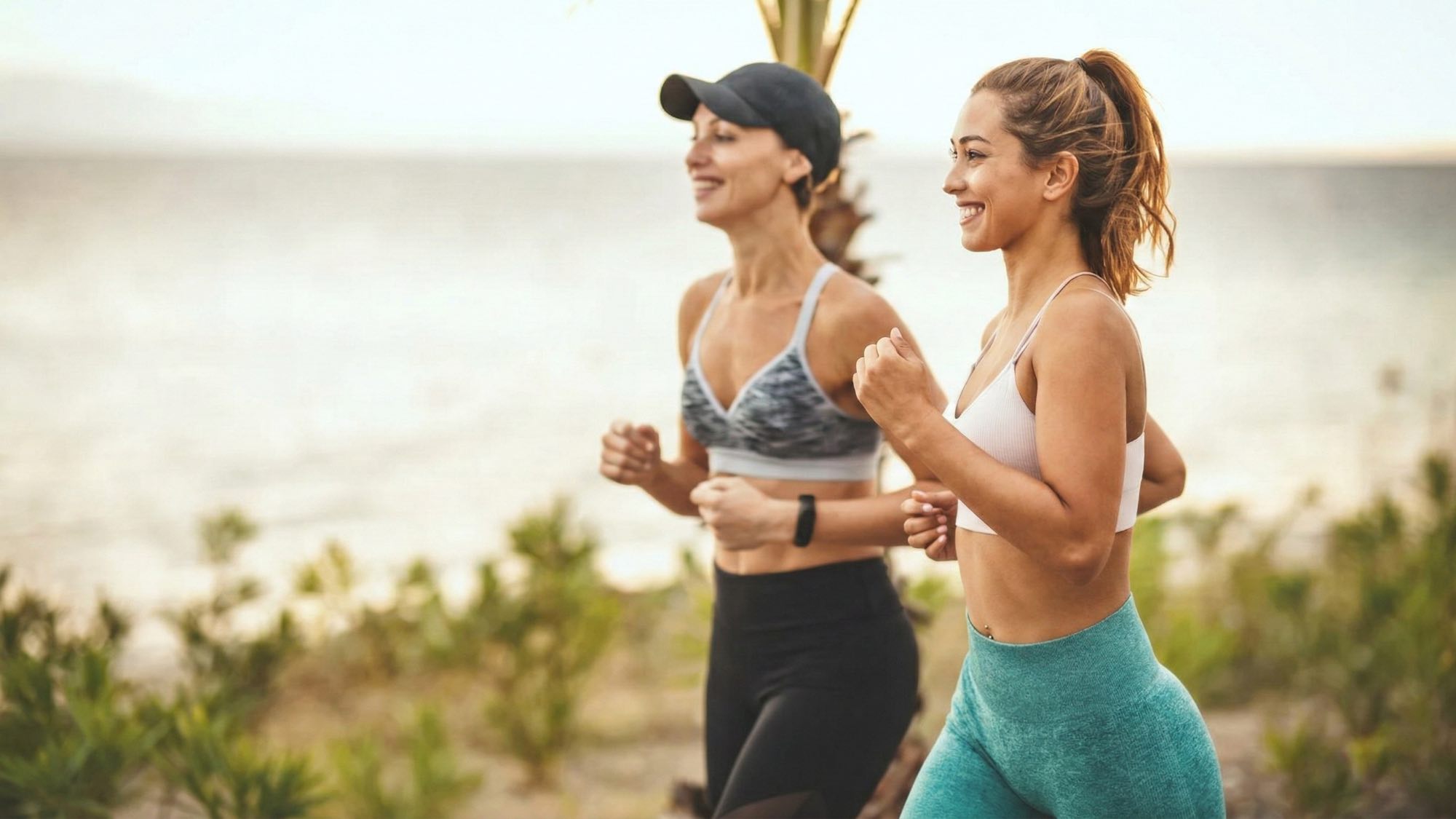 Two women power walking outdoors by the ocean smiling 