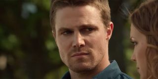 Arrow's Stephen Amell sitting on a park bench and having a conversation, looking solemn.