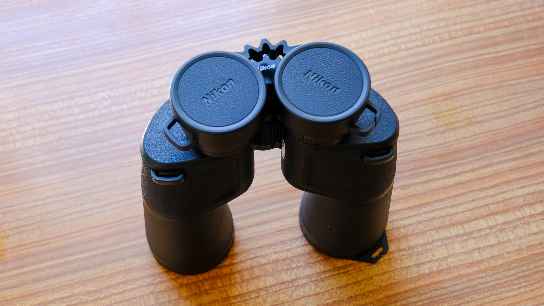 The Nikon Action 7x50 binoculars stood up on a wooden table with eyecup covers on.