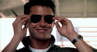 Tom Cruise as Maverick, smiling with sunglasses on, in Top Gun