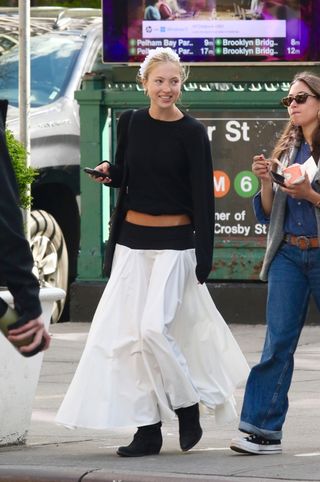 Lyla Moss wears a low-rise white skirt and a black cropped sweater