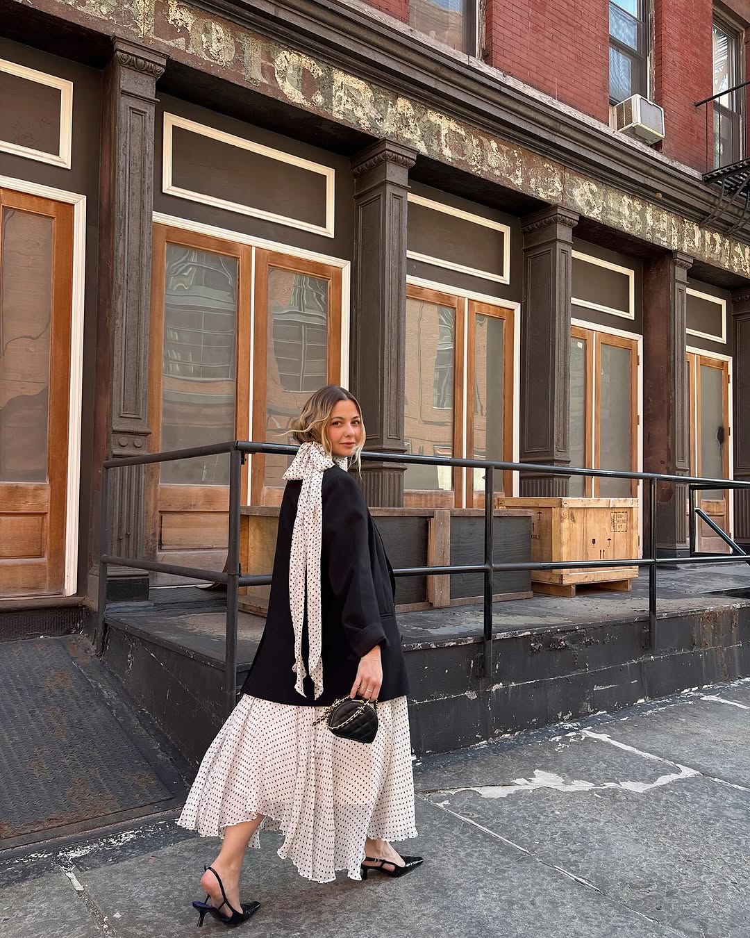 Influencer Olivia Marcus in a full lenght polka dot dress black sling back heels a black blazer and mini Chanel pouch bag.