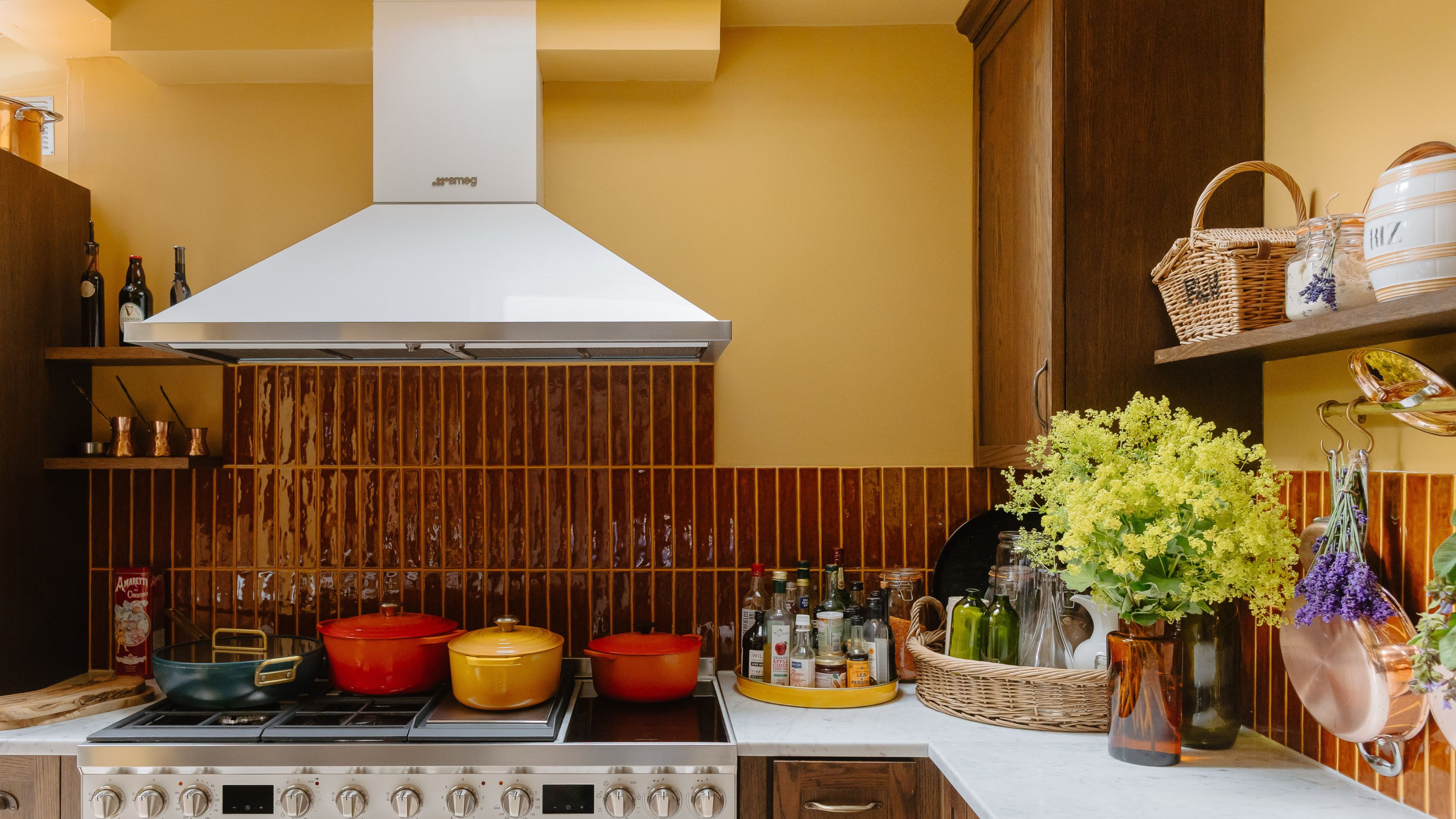 Clodagh McKenna's kitchen with painted yellow walls, burgundy tiles, a marble countertop, wooden cabinets, and a stainless steel range hood