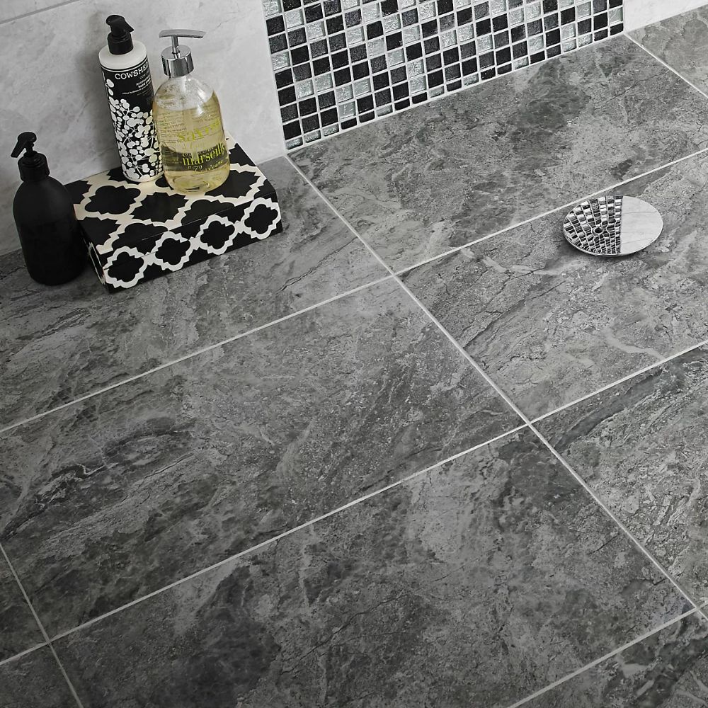 A close-up of a modern bathroom floor featuring anthracite grey travertine-effect ceramic tiles.