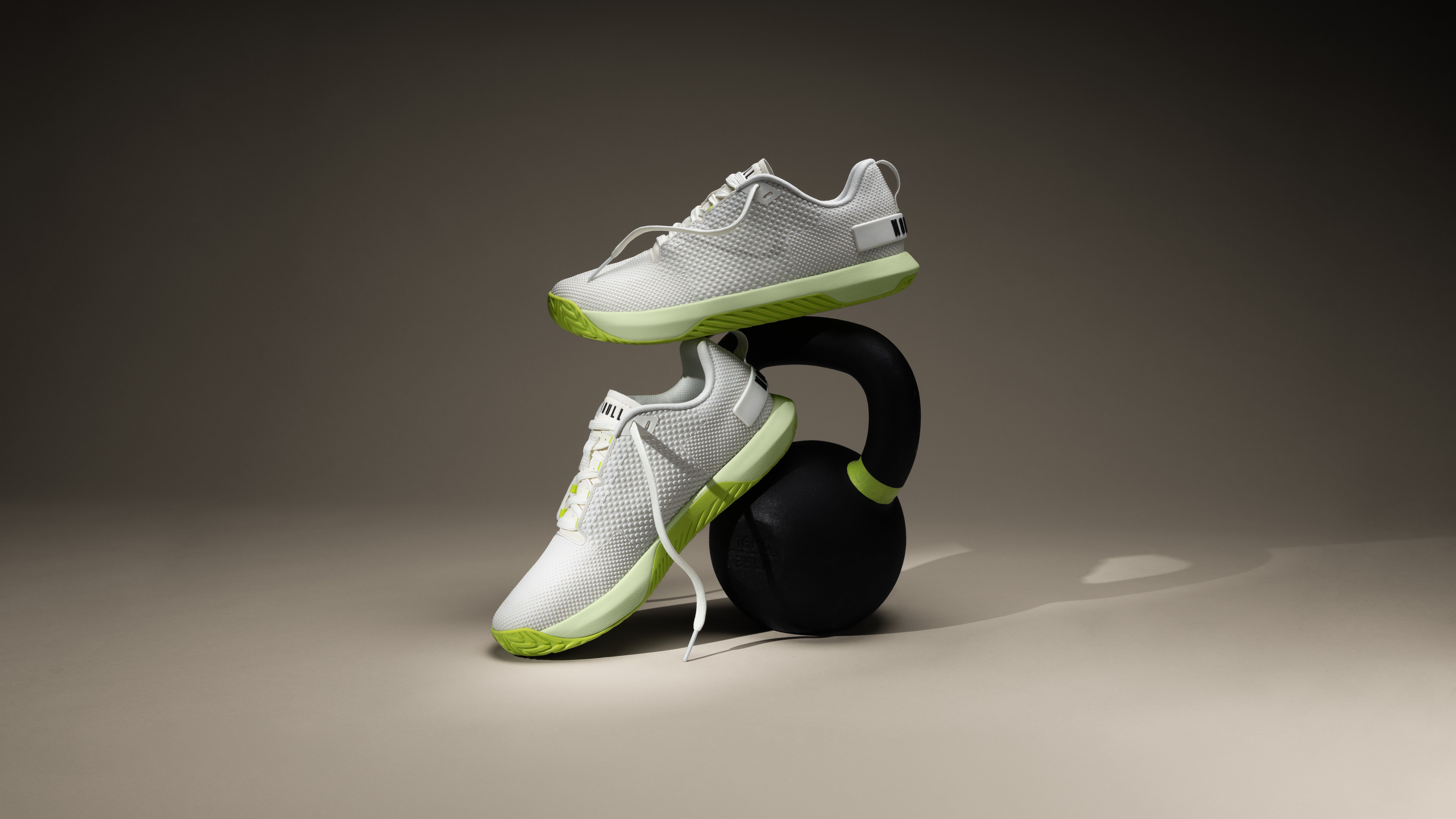 NOBULL Outwork cross training shoes in white and green, displayed on a kettlebell