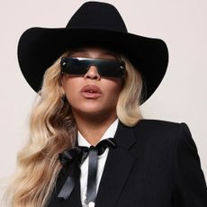 Beyonce stands in front of a plain backdrop wearing a cowboy hat and a black suit