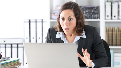 A businesswoman looks shocked as she looks at her laptop in her office.
