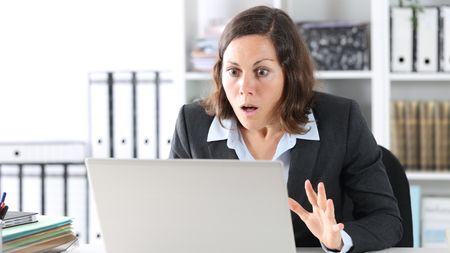A businesswoman looks shocked as she looks at her laptop in her office.