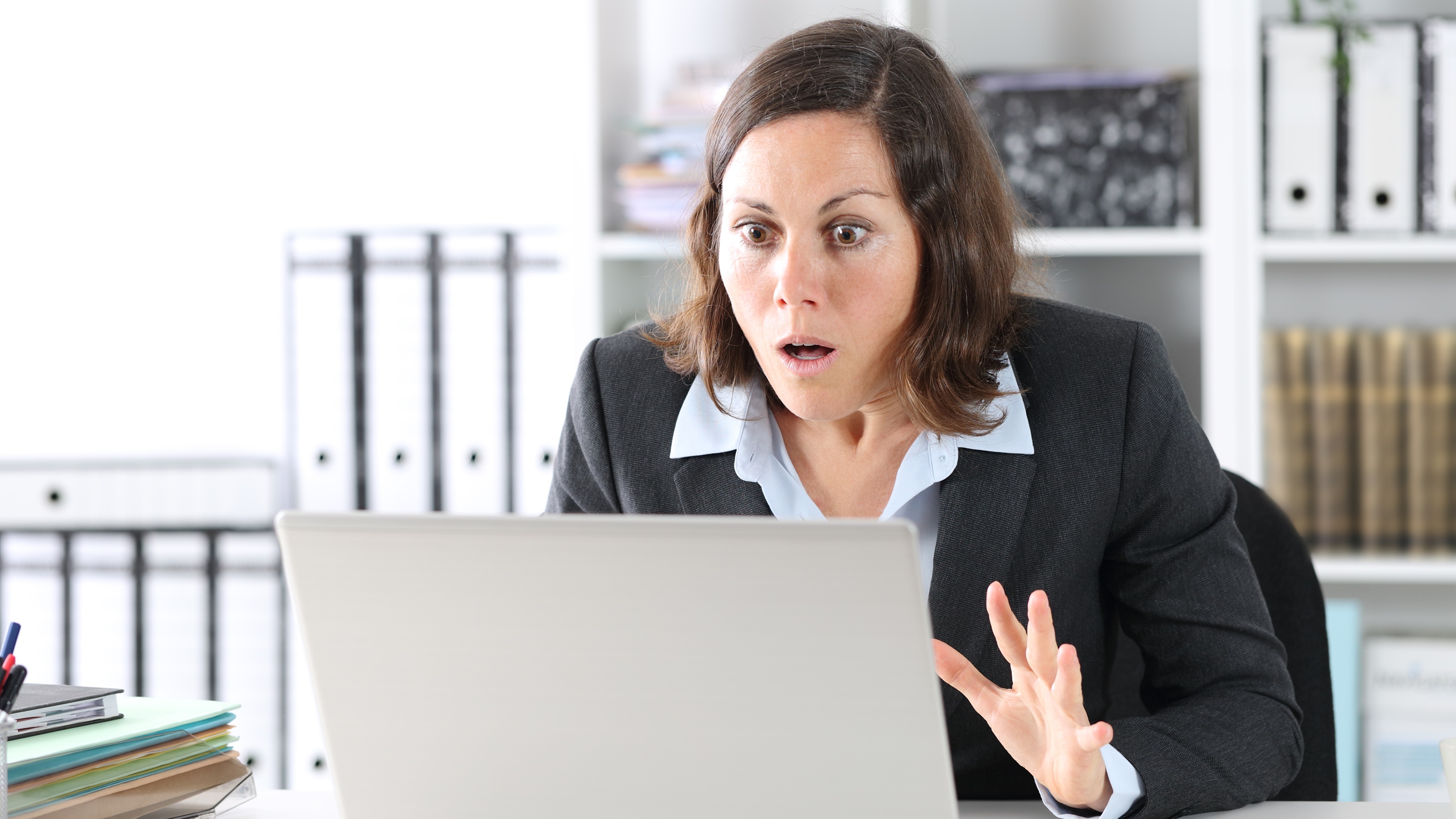 A businesswoman looks shocked as she looks at her laptop in her office.