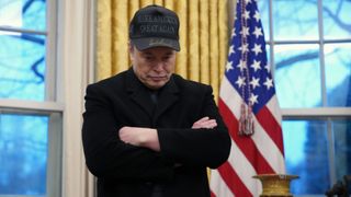 Elon Musk stood in the White House with his arms folded and his head down looking tired