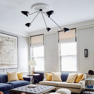 White living room with blue and cream sofas, ottoman and black sculptural ceiling light