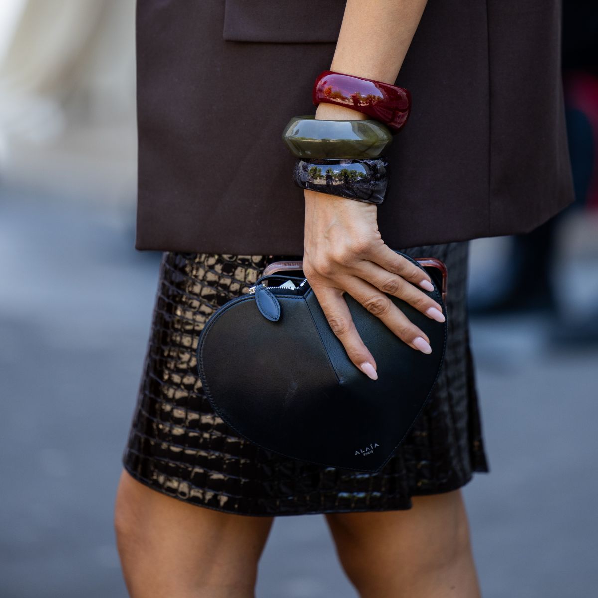 Woman holding a clutch bag, wearing three large bangles with soft serve nails