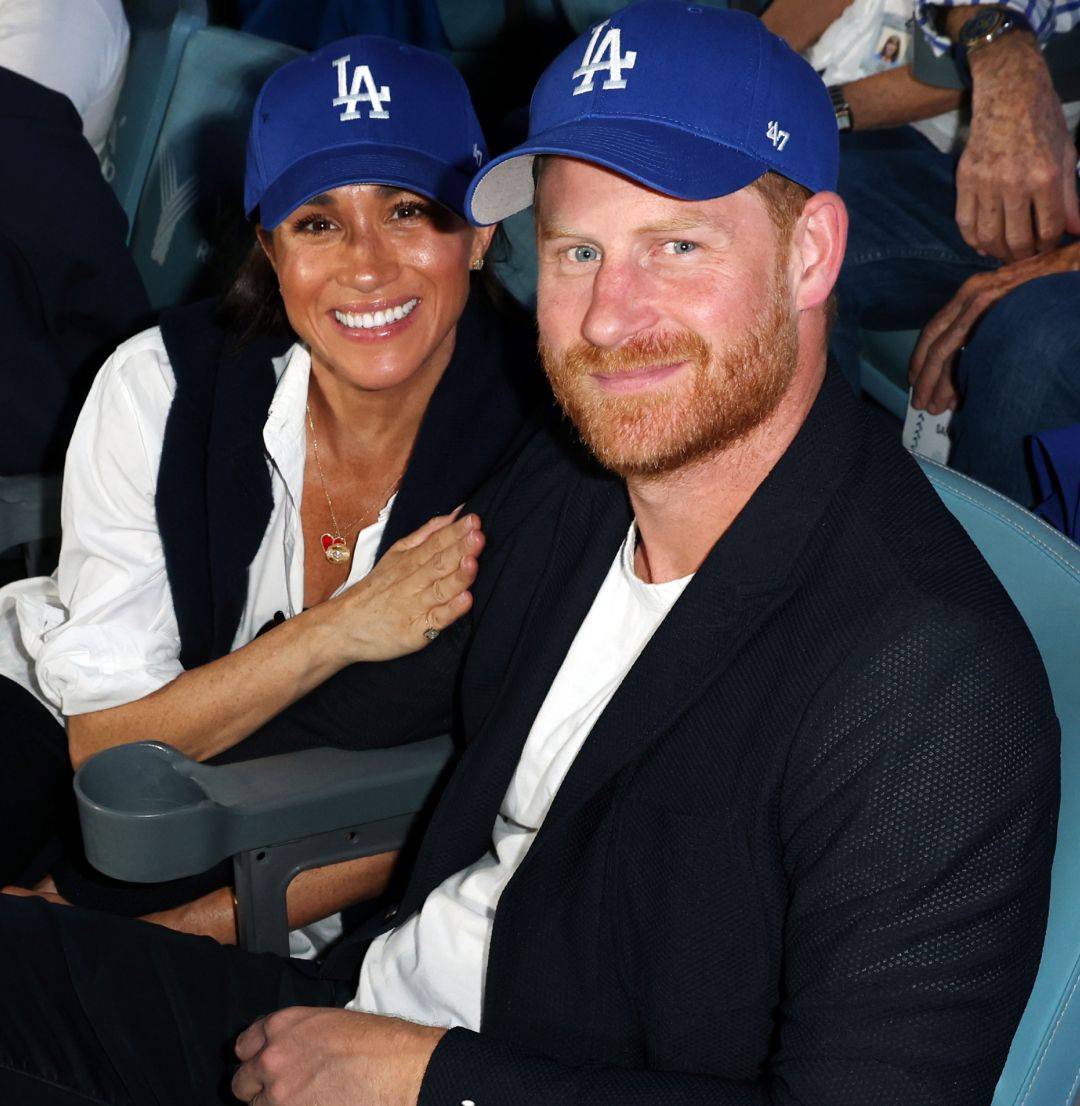 Meghan Markle and Prince Harry sitting in seats wearing Dodgers hats at the World series