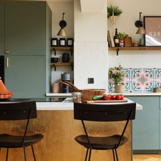 kitchen island with gold covering with set of stools, in front of green cabinets and white worktops