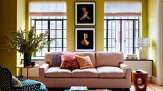 A modern living room with chartreuse walls, a white ceiling, two large windows, a pink sofa with colorful cushions and a modern multi-colored glass coffee table. 