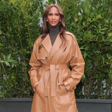 Supermodel, Iman, wearing a turtle neck shirt under a trench coat. She has long, curled hair, and is looking into the camera.
