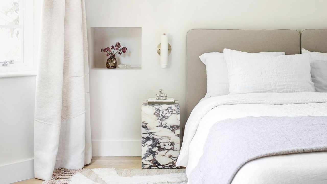 A contemporary white bedroom with a marble bedside table and bed dressed in white bedding