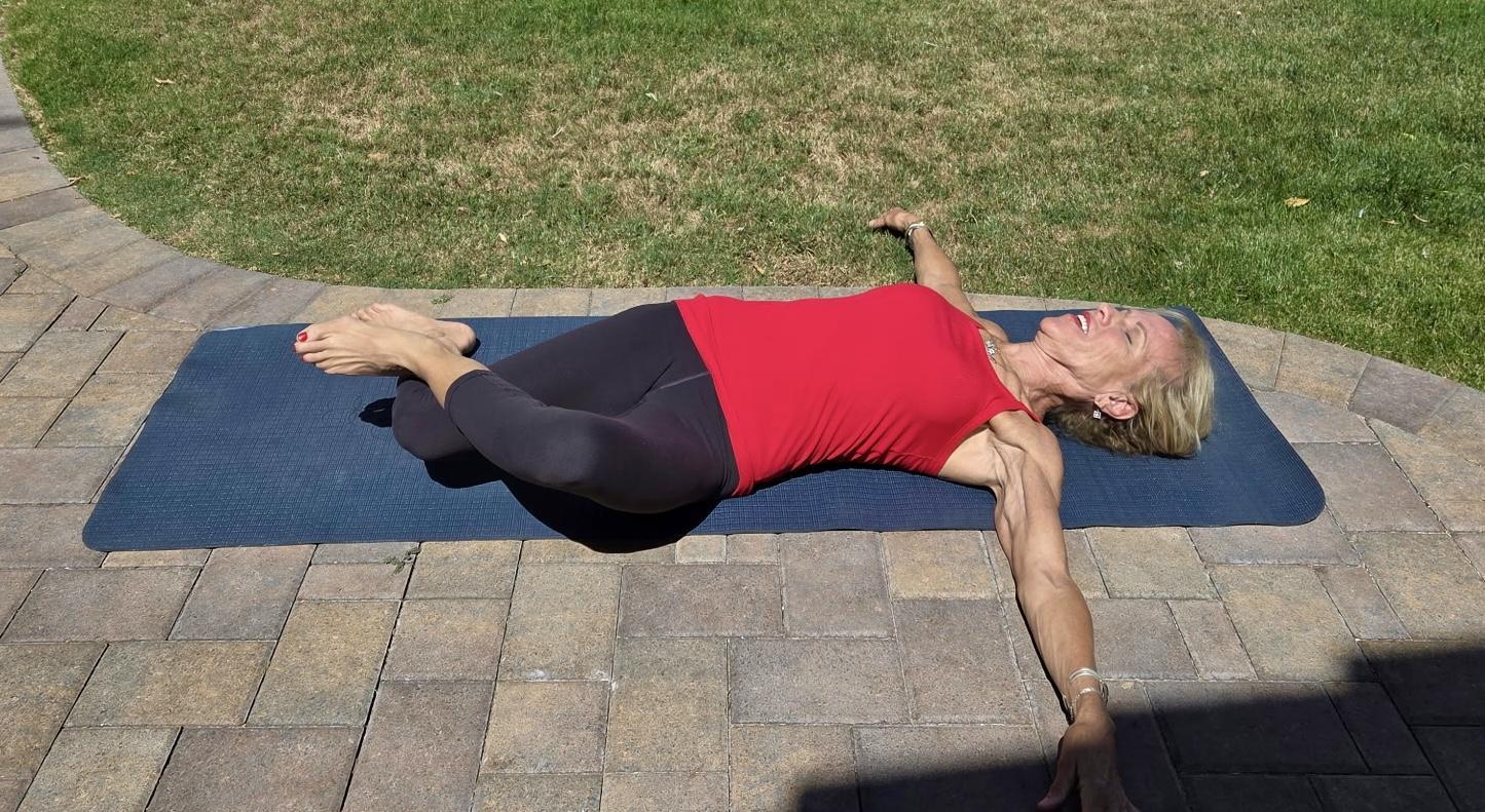 Woman in black leggings and red tank top on exercise mat on patio outside, next to grass.
