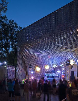 Metal cube with once side drawn back to reveal a stage with lights