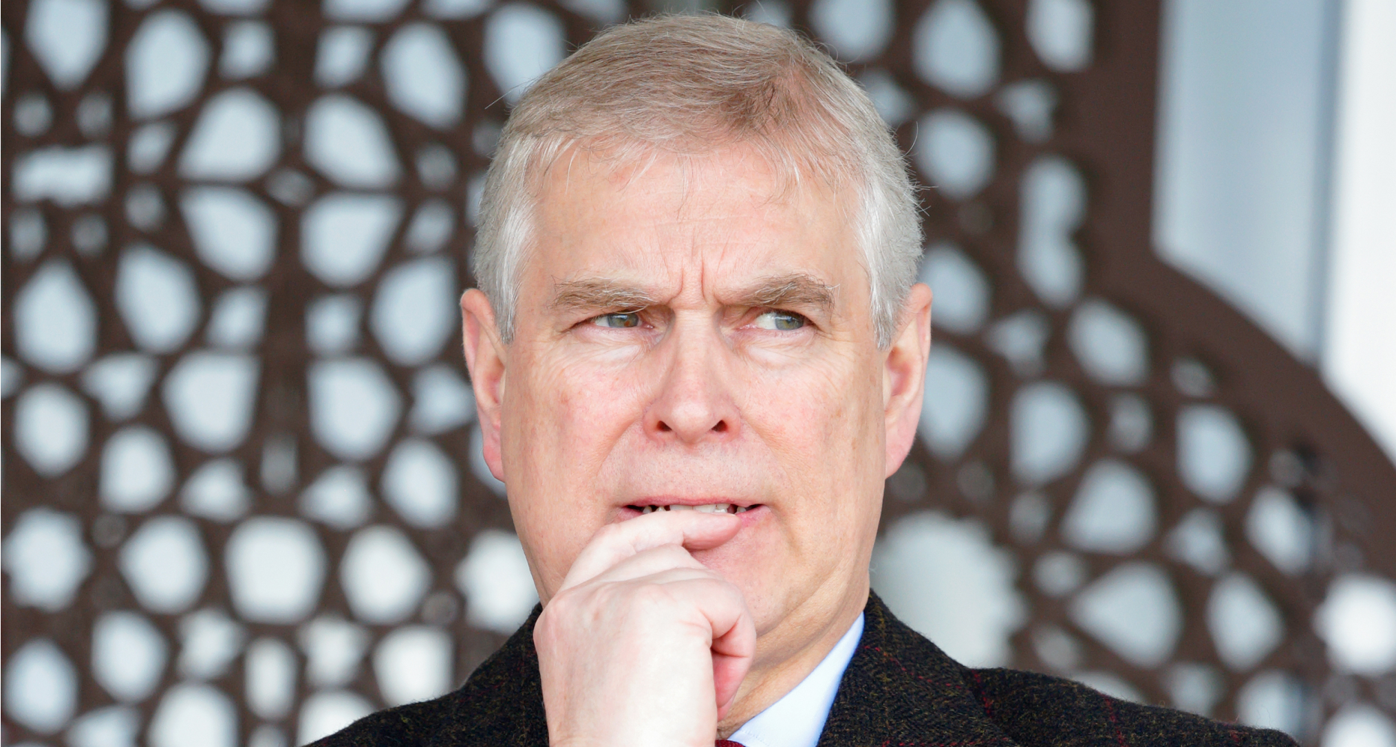 Prince Andrew wearing a suit putting his finger to his mouth