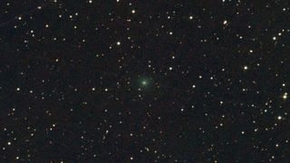 A bright green light faintly glows in the center of a dark starry night sky