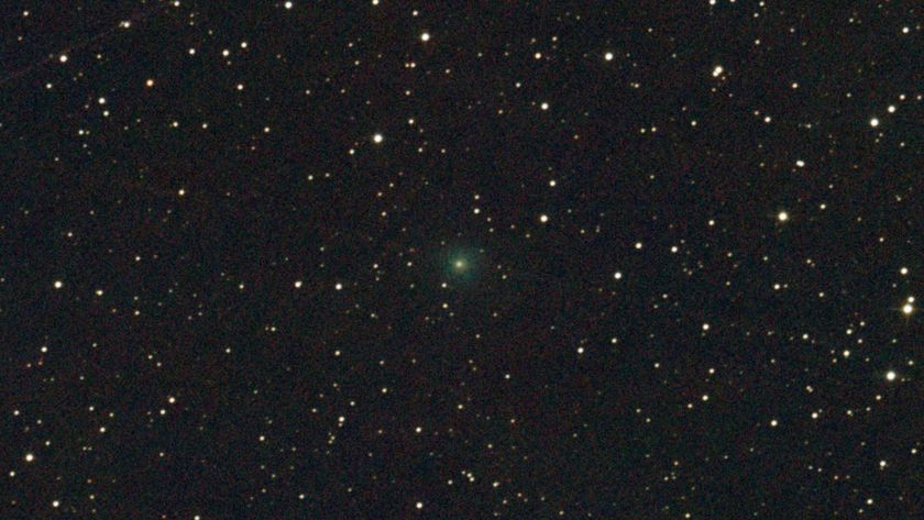 A bright green light faintly glows in the center of a dark starry night sky