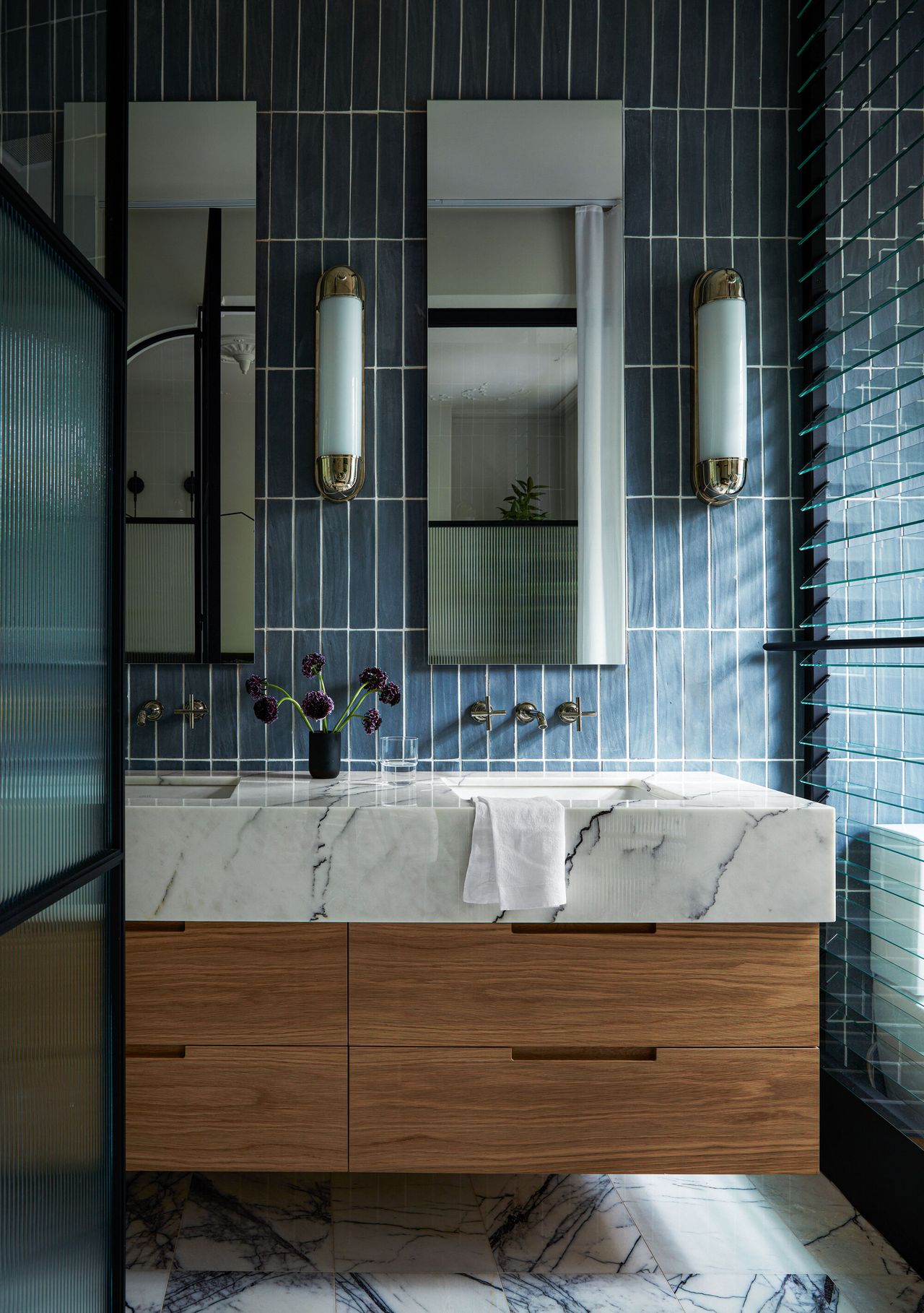 A blue tiled bathroom with a marble sink and glass shutters