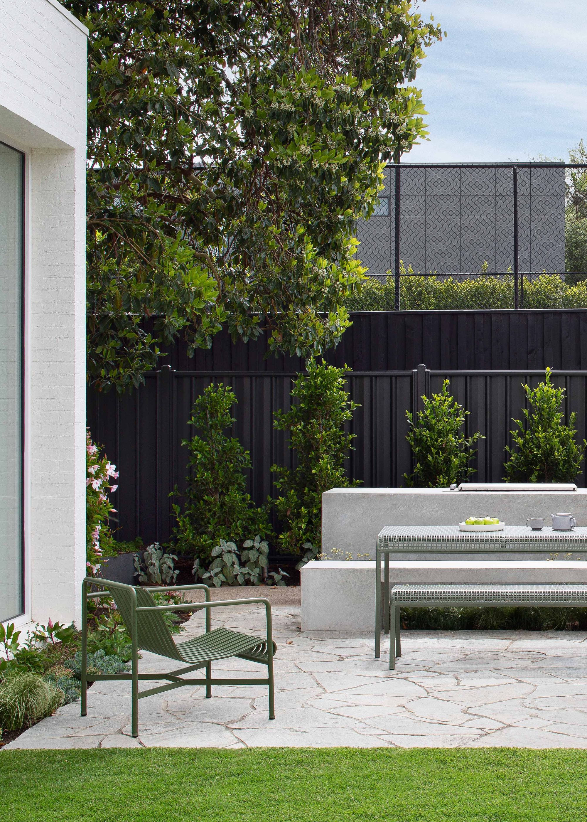 A garden with black fencing and metal lawn furniture