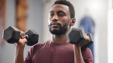 Man in gym lifting weights up to shoulder height