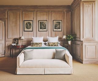 cream sofa at the end of bed in room with wooden walls