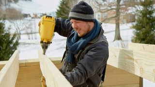 Caucasian man nailing timbers outside in snow