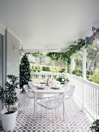 Christmas patio/porch with dining table, Christmas tree, garland, white table and chairs, gray and white tiled floor