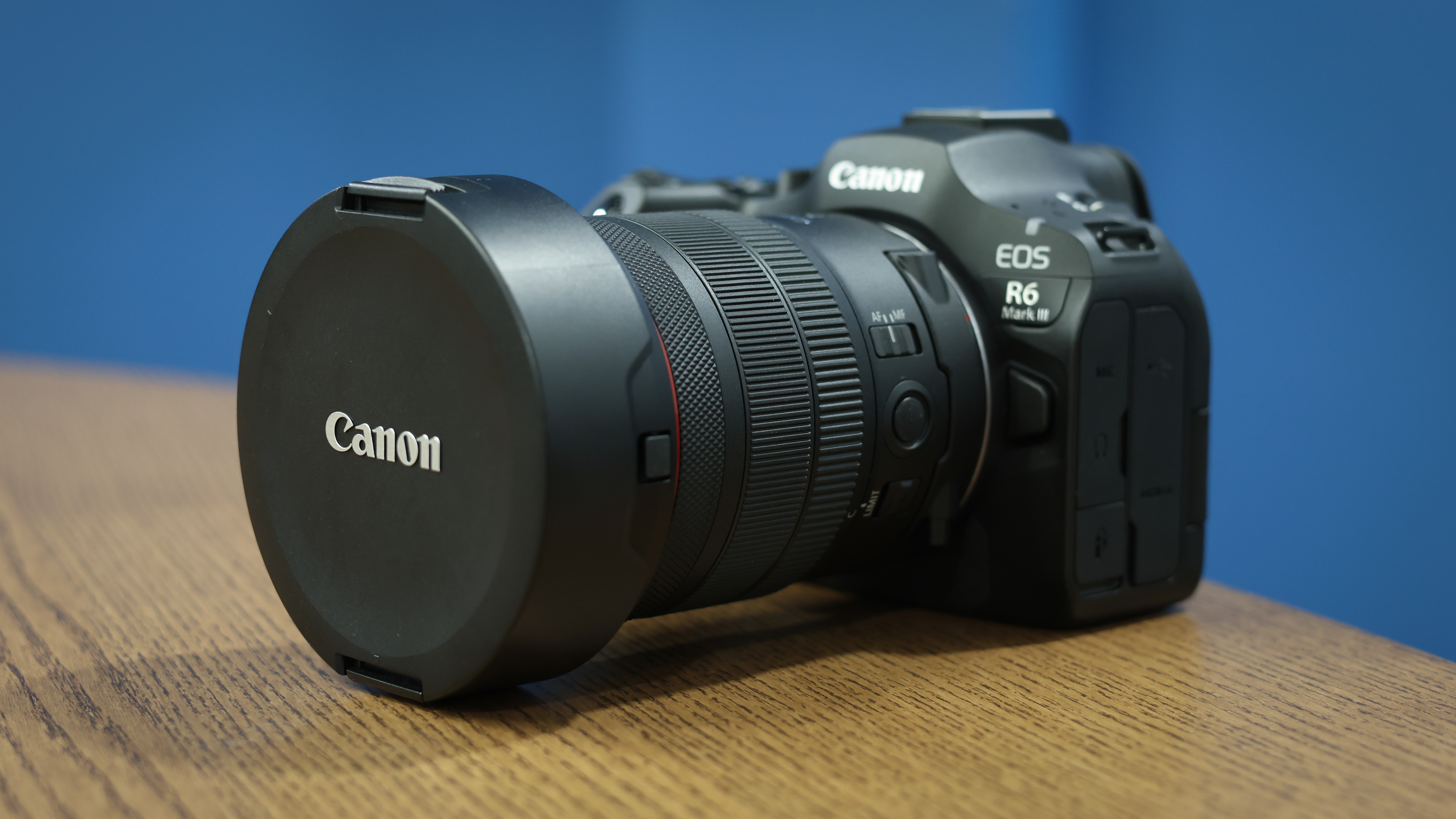 Canon RF 7-14mm f/2.8-3.5L Fisheye STM on a wooden surface in front of a blue background