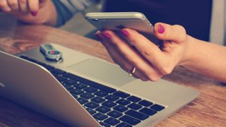 Woman holding smartphone with a MAC laptop in front of her 