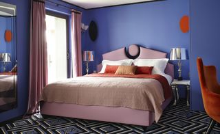 Hotel room with blue walls, patterned carpet and pink bed