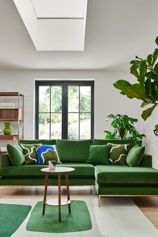 A living room with a green velvet sofa and geometric patterned cushions, and a color blocked rug