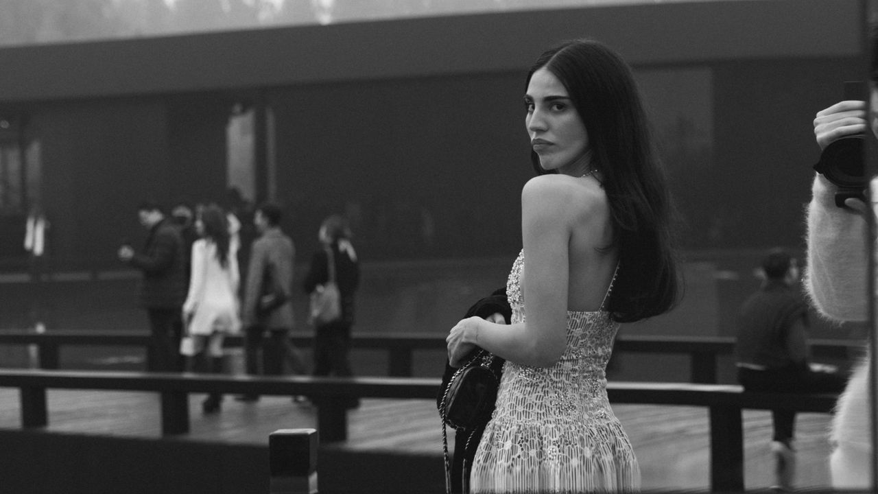 Writer Orion Carloto attends the Chanel Metiers D&#039;Art Show wearing a sparkly Chanel dress with white pumps and a black Chanel bag